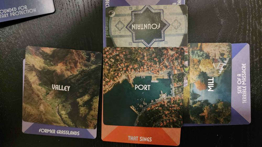 Story Engine deck cards, from the worldbuilding deck.
Left: Valley (Former grasslands)
Middle: Port (that sings)
Upper Middle: Fountain (created as a gift, which is offscreen here)
Right: Mill (site of a terrible massacre)